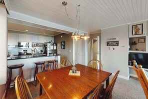 A dining area with a wooden table and chairs, a kitchen with white cabinets, and a ceiling light fixture.