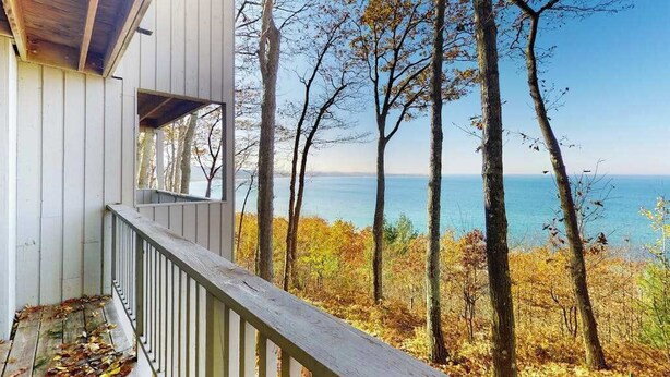 A wooden deck with a railing overlooking a body of water and trees. - Tasteful Glen Arbor condo with beautiful Lake Michigan views, deck & fireplaces (Glen Arbor)