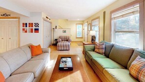 Ein Wohnzimmer mit grauem Sofa, grünem Sofa, Sesseln im Karomuster und einem Couchtisch.