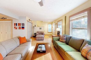 Ein Wohnzimmer mit grauem Sofa, grünem Sofa, Sesseln im Karomuster und einem Couchtisch.