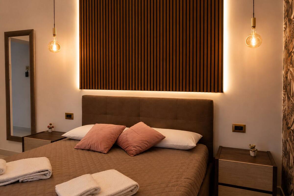 Quarto moderno com uma cama grande, duas mesas de cabeceira, um espelho e um aplique na parede.