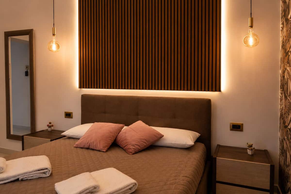 A modern bedroom with a large bed, two bedside tables, a mirror, and a wall-mounted light fixture.