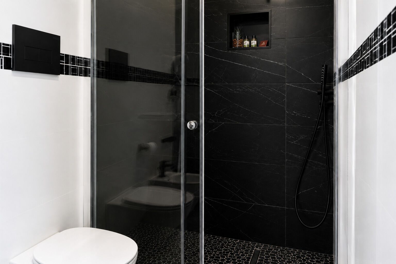 Une salle de bain moderne avec une douche à parois de verre, des toilettes et une petite étagère contenant des articles de toilette.