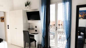 Habitación de hotel con cama, escritorio, silla, televisor y balcón con vista a la ciudad.