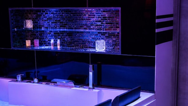 Un moderno espacio de spa con un amplio jacuzzi, un panel de vidrio y un estante con diversos objetos.