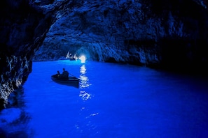 A boat in a cave with a light at the end. - Vesun Suites (Naples)