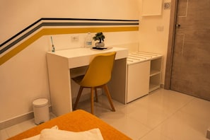 A small, modern hotel room with a desk, chair, and a bed with an orange headboard. - Vesun Suites (Naples)