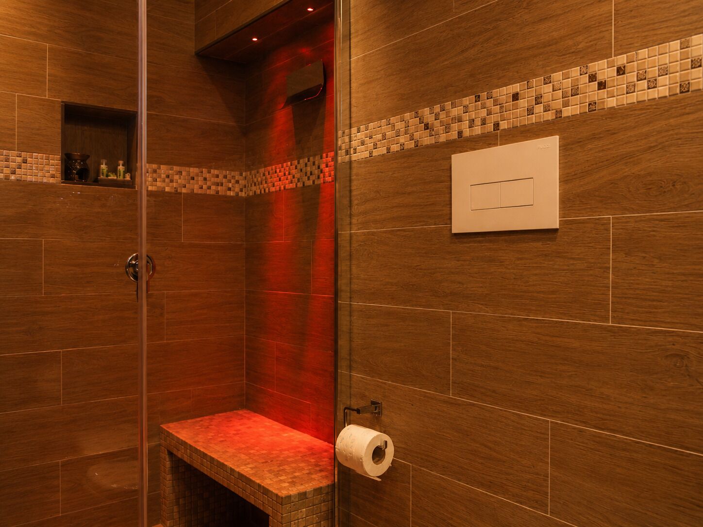 Eine Dusche mit Glastür, eine Sitzbank und einem Toilettenpapierhalter.