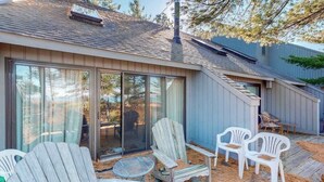A patio with Adirondack chairs, a small round table, and a sliding glass door leading to a covered area. - Beachfront townhouse & loft near the water with firepit, deck & cable (Glen Arbor)