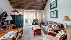 A cozy living room with a wooden ceiling, a green cabinet, a sofa with patterned cushions, a wooden coffee table, and a dining table with chairs. - Beachfront townhouse & loft near the water with firepit, deck & cable (Glen Arbor)