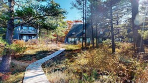 A wooden pathway leading to a modern cabin surrounded by trees. - Beachfront townhouse & loft near the water with firepit, deck & cable (Glen Arbor)
