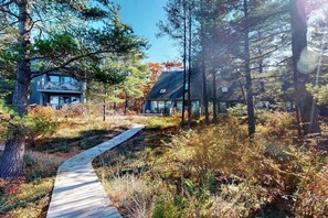 Un sentier en bois mène à un chalet moderne entouré d’arbres.