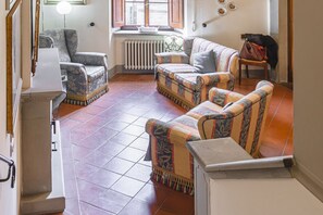 Ein Wohnzimmer mit gestreiften Sofas, einem Heizkörper, einem Fenster mit Rollläden und einer Treppe.