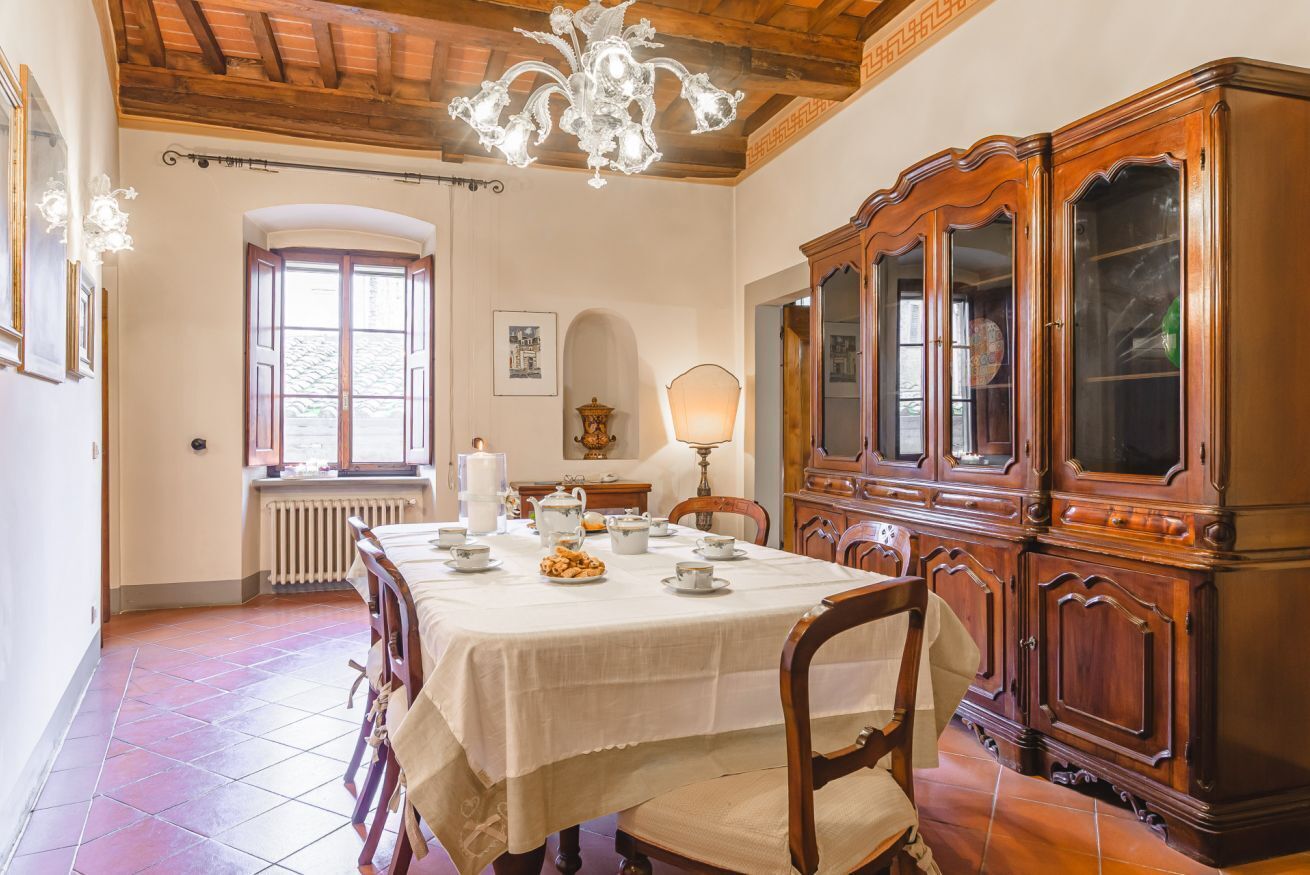A dining room with a wooden table set for four, a chandelier, and a large wooden cabinet with glass doors.