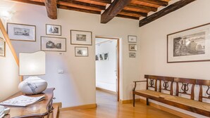 A room with wooden floors, a bench, a desk with a lamp, and framed pictures on the walls. - Palazzo Simonetti - a noble elegance in the heart of Cortona (Cortona)