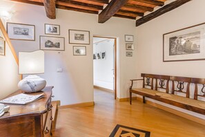 A room with wooden floors, a bench, a desk with a lamp, and framed pictures on the walls. - Palazzo Simonetti - a noble elegance in the heart of Cortona (Cortona)