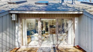 Een klein, gelijkvloers gebouw met een schuifdeur van glas, een overdekt terras en zichtbaar interieur met meubels.