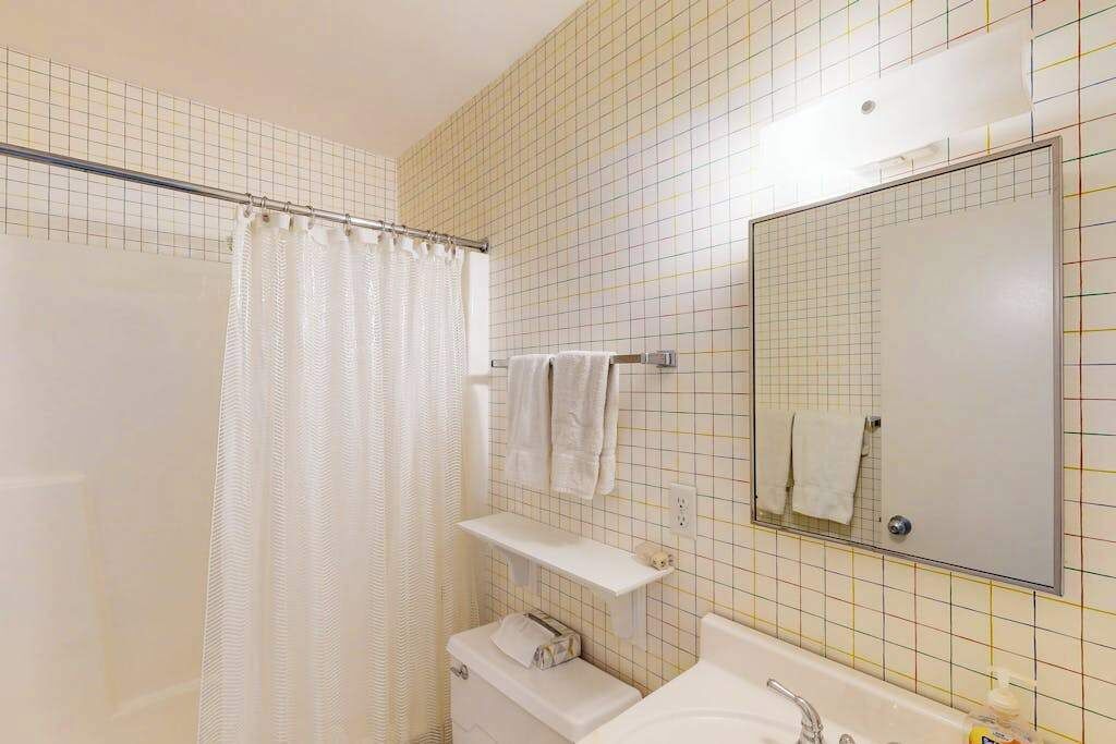 Un baño con cortina de ducha, lavamanos, espejo y toallero.