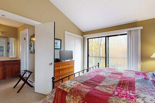 A bedroom with a bed, dresser, television, and a balcony with a view.