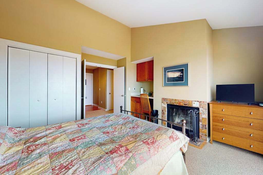 Une chambre à coucher comprenant un lit, une commode, un téléviseur, une cheminée et un couloir menant à une salle de bain.