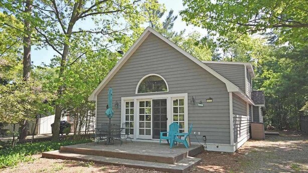 A small, single-story house with a porch, a covered patio, and a garage. - Charming home near the lake with a fireplace, central AC, washer/dryer & grill (Glen Arbor)