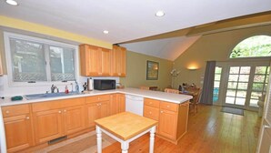 A kitchen with wooden cabinets, a microwave, and a dining area with chairs. - Charming home near the lake with a fireplace, central AC, washer/dryer & grill (Glen Arbor)