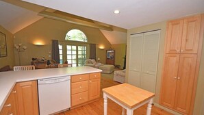 A kitchen with wooden cabinets, a dishwasher, a dining table, and a large window with a view. - Charming home near the lake with a fireplace, central AC, washer/dryer & grill (Glen Arbor)