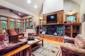 A spacious living room with a fireplace, comfortable seating, and large windows.