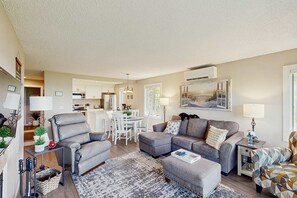 Ein Wohnzimmer mit grauem Sofa, einem gemusterten Teppich und einem Essbereich mit weißem Tisch und Stühlen.