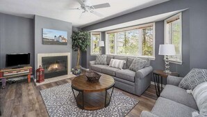 Ein Wohnzimmer mit Kamin, grauen Sofas, einem Couchtisch und einem Fernseher.