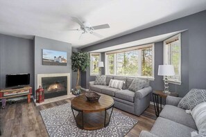 Ein Wohnzimmer mit Kamin, grauen Sofas, einem Couchtisch und einem Fernseher.