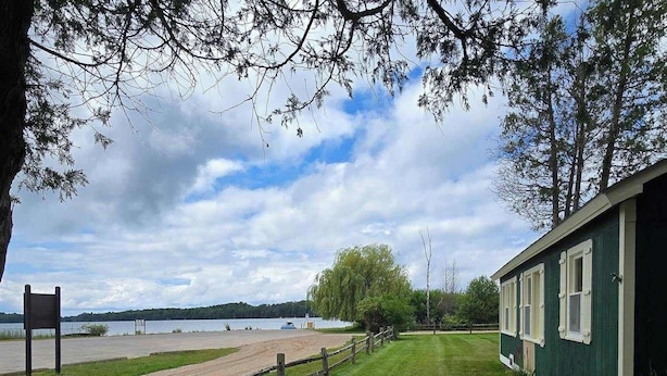 Ett grönområde med ett trästaket, en byggnad med fönster och en vattenyta i bakgrunden.