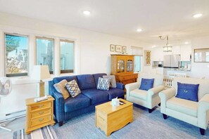 A living room with a blue sofa, a wooden coffee table, a white armchair, and a cabinet. - Beachfront condo in Glen Arbor with deck, fireplace, Lake Michigan views & W/D (Glen Arbor)