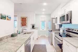A modern kitchen with granite countertops, stainless steel appliances, and white cabinetry. - Beachfront condo in Glen Arbor with deck, fireplace, Lake Michigan views & W/D (Glen Arbor)
