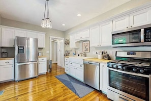 A modern kitchen with stainless steel appliances, white cabinetry, and a wooden floor.