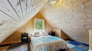 A bedroom with a sloped ceiling, a bed with a patterned bedspread, two bedside tables, and a window. - Arcadia Retreat w/ private hot tub, gas grill, fire pit, near beach, Dogs- YES! (Arcadia)