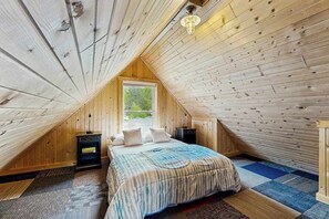 A bedroom with a sloped ceiling, a bed with a patterned bedspread, two bedside tables, and a window.