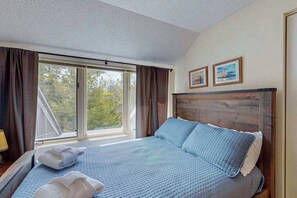 Ein Schlafzimmer mit großem Fenster, einem Bett mit blauer Bettwäsche und zwei gerahmten Bildern an der Wand.