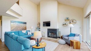A modern living room with a sofa, a TV, a fireplace, and a large window. - Darling condo on Lake Michigan with washer/dryer, deck, lake views, fireplace (Glen Arbor)