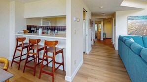 A modern kitchen with a bar area, wooden chairs, and a blue sofa in a spacious living area. - Darling condo on Lake Michigan with washer/dryer, deck, lake views, fireplace (Glen Arbor)