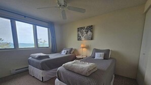 A bedroom with two beds, a ceiling fan, a window with a view, and a wall-mounted lamp. - Darling condo on Lake Michigan with washer/dryer, deck, lake views, fireplace (Glen Arbor)