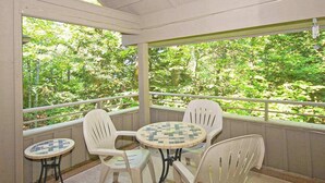 Un balcon abrité, doté d’une table et de chaises, entouré de murs blancs et de grandes fenêtres donnant sur une forêt.
