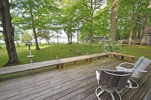 Eine Holzterrasse mit Bänken und Stühlen, umgeben von Bäumen und Blick auf einen See.