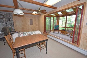 Ein Holzespeisesaal mit Stühlen, eine Couch und ein Deckenventilator in einem Raum mit großen Fenstern und einer Steinwand.