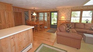 A spacious living area with a dining table, wooden cabinets, and a sofa. - Lakefront home on Little Glen Lake with fireplace, deck, gas grill, and firepit (Empire)