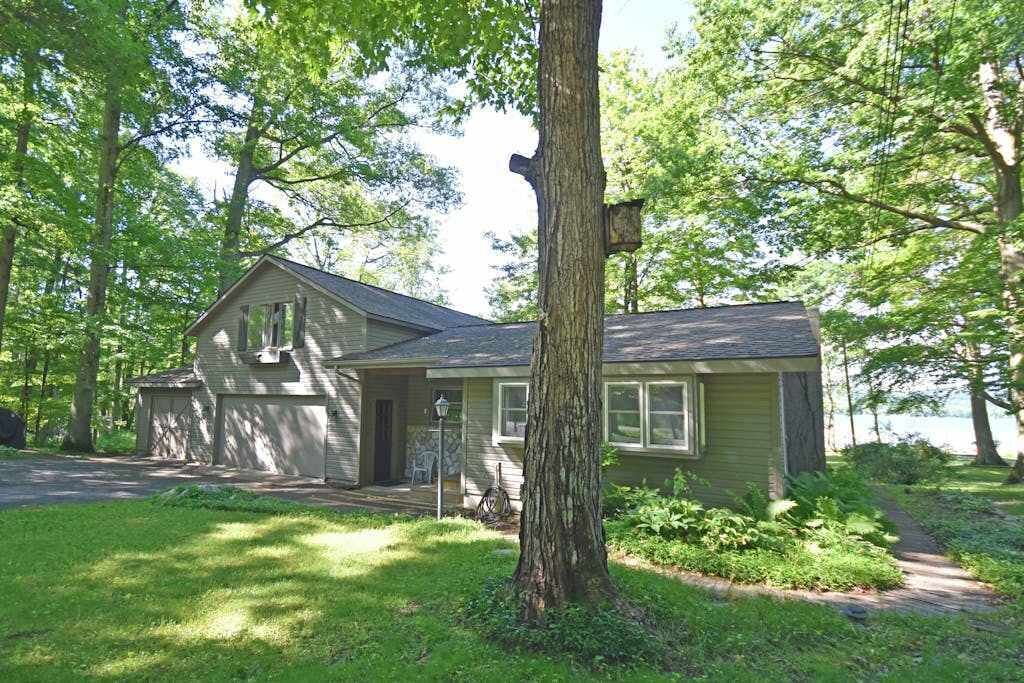 A single-story house with a garage, surrounded by trees and a grassy yard.