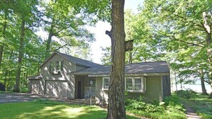 A single-story house with a garage, surrounded by trees and a grassy yard. - Lakefront home on Little Glen Lake with fireplace, deck, gas grill, and firepit (Empire)