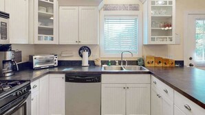 Una cocina con armarios blancos, un tostador, un lavamanos y una ventana con persianas.