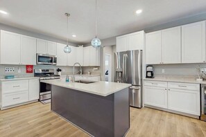 A modern kitchen with white cabinets, stainless steel appliances, and a central island. - Modern Harbor County Home w/ hot tub, ping-ping, patio, grill, & walk to beach! (Union Pier)