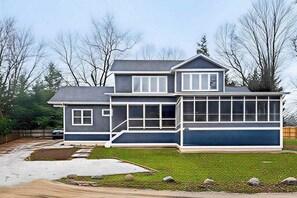 A two-story house with a large front porch, a garage, and a well-maintained lawn. - Modern Harbor County Home w/ hot tub, ping-ping, patio, grill, & walk to beach! (Union Pier)